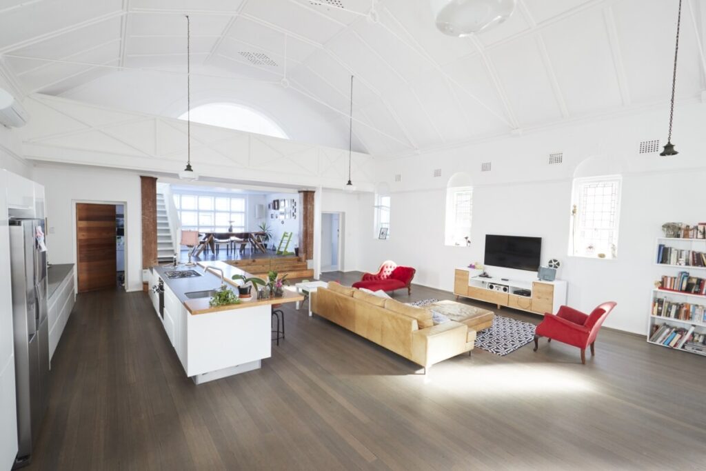 Architekt wnętrz prezentuje otwartą przestrzeń z podłogą drewnianą, białym sufitem i wyspą kuchenną